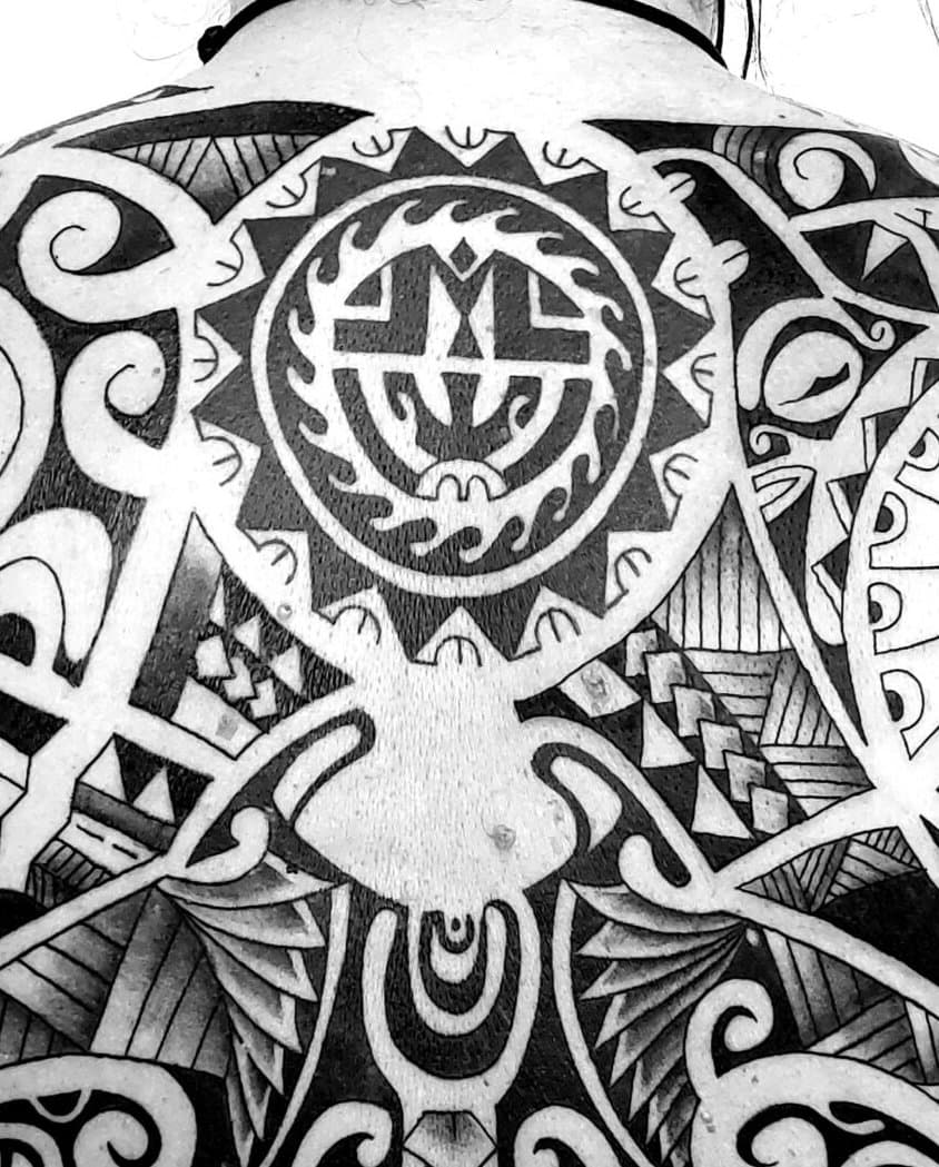 Polynézsky blackwork cez celý chrbát — slnečný disk medzi lopatkami, manta a žralok schádzajúci po chrbtici, ornament pokrýva chrbát až po kríže — detail 1