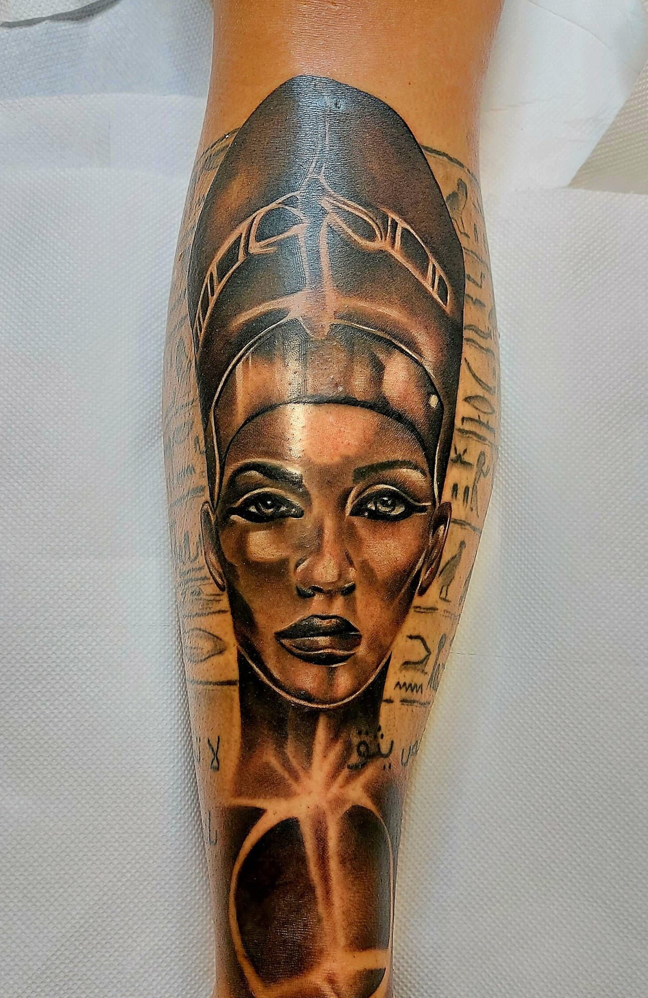 Realistická busta Nefertiti s hieroglyfmi a ankhom cez celé lýtko, v teplých sépiových tónoch